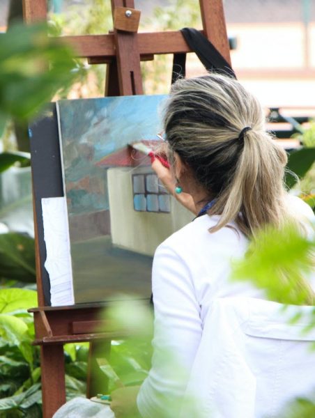 Frau malt im Freien ein Bild mit Acrylfarben und Pinsel