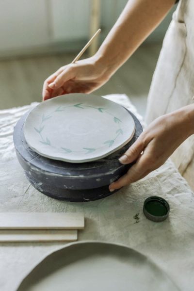 woman hand painting a ceramic plate with ceramic colors and an artist brush